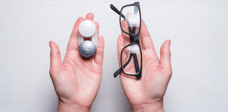 One hand holding a pair of glasses, the other holding contact lenses