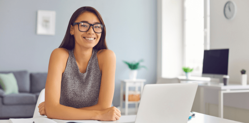 A woman wearing glasses at the desk with a laptop
