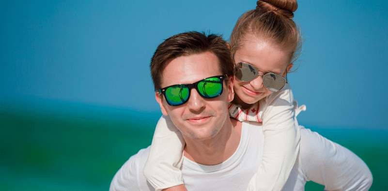 A father giving his daughter a piggyback, both wearing sunglasses outside