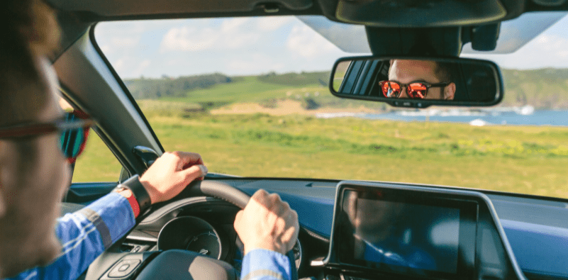 A man driving on a bright day in the countryside, wearing sunglasses